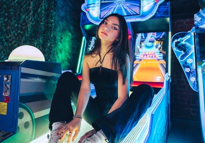 A person sitting on an arcade game machine platform with neon lights in the background. The arcade game is called 'Lane Master' and features a colorful design with bowling-themed imagery.
