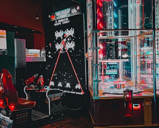 An arcade setting featuring a classic Space Invaders game setup and a modern gaming machine with seats. Bright neon lights illuminate the area, with scores displayed on digital screens. A bright and visually engaging environment full of electronic components.